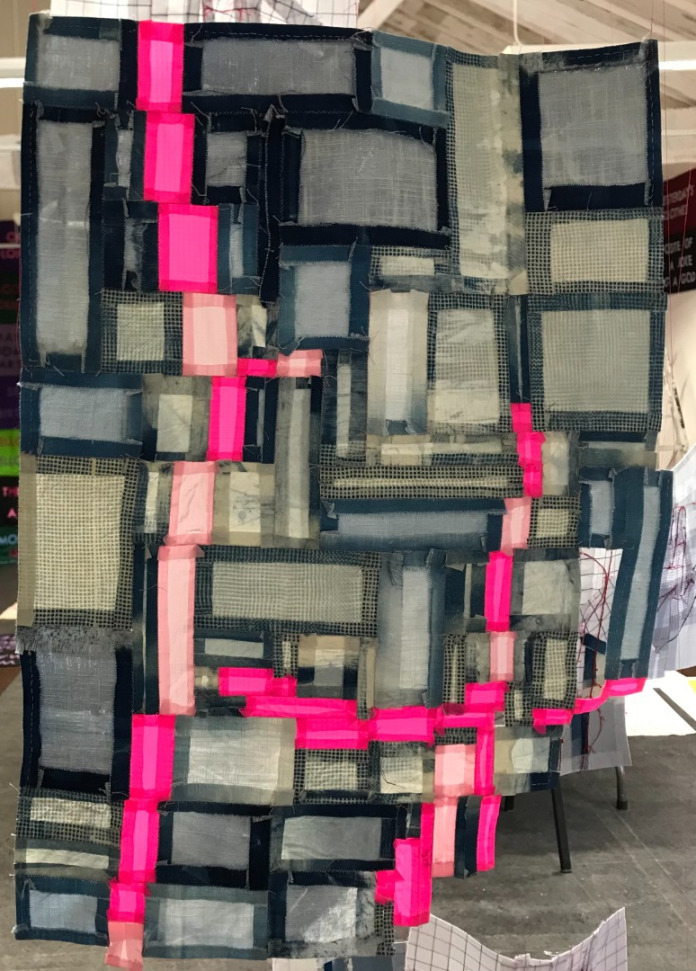 Title: Curvy Hip and Bum. A textile piece made from irregularly sized rectangles of blue linen, and bright pink nylon. The pink pieces create an abstracted outline of a person's curvy waist and bum. The piece is lit from the front meaning the hems of each small fabric rectangle shows as a neat, dark border to each patch. 