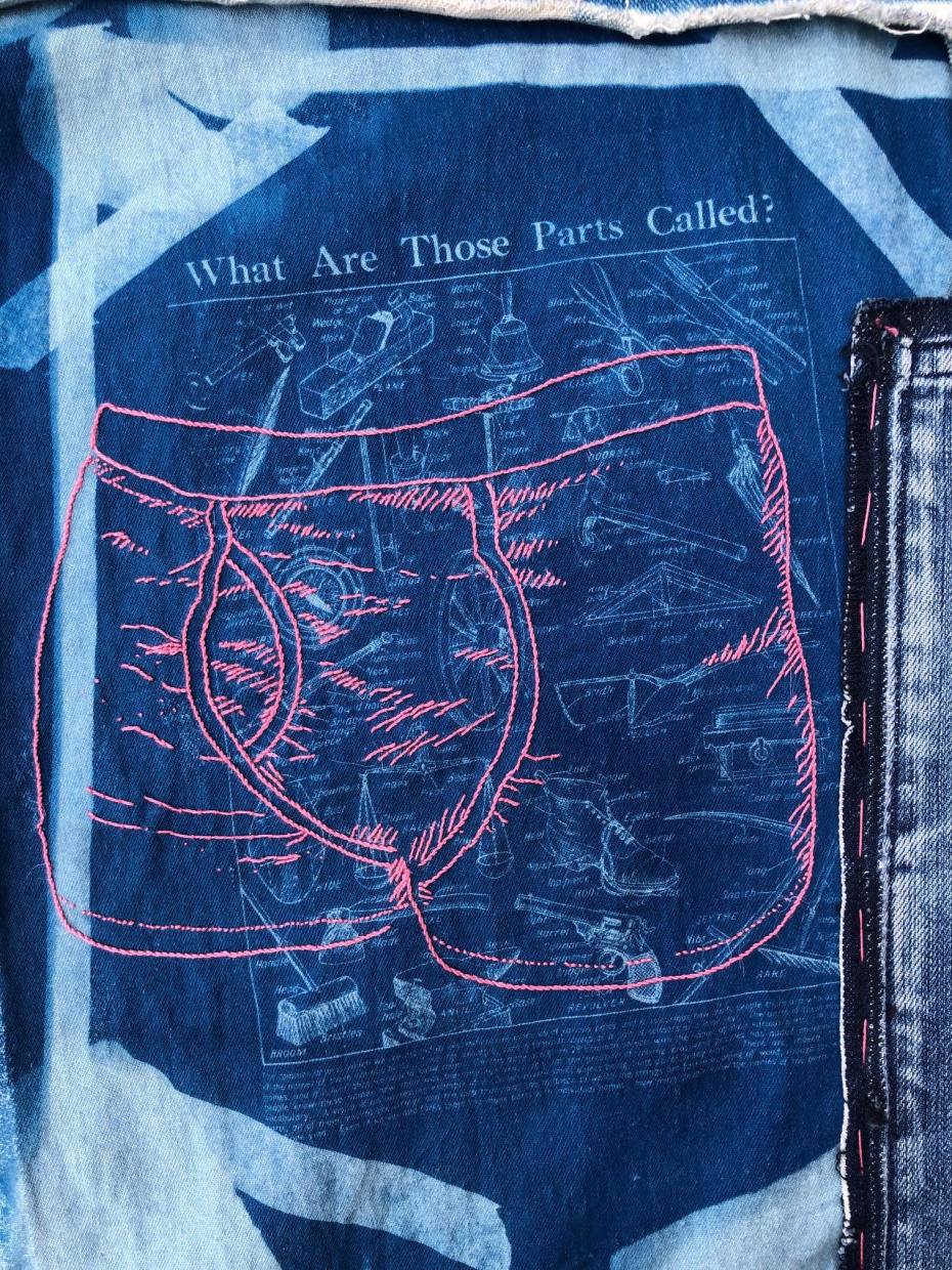 A photo of a piece of embroidery on printed denim. The print is in pale and deep blue, taken from a 1930s magazine illustration titled "what are those parts called?" with line drawings of labelled domestic tools and machinery. The embroidery stitched over the print is a pair of men's pants in thick pink thread. 